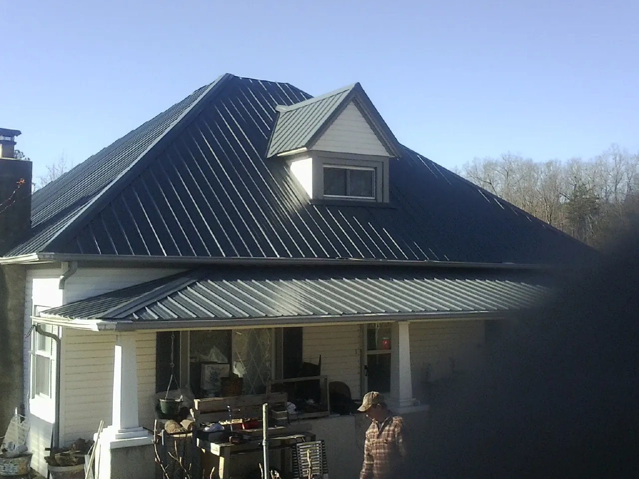 Dark blue standing seam metal roof with a dormer above a front porch in Shawano