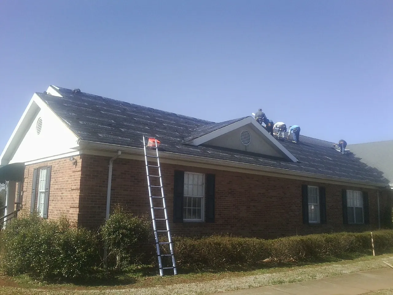 Crew tearing shingles off a brick ranch roof with a ladder set — Emergency Roof Repair work by our crew in Shawano