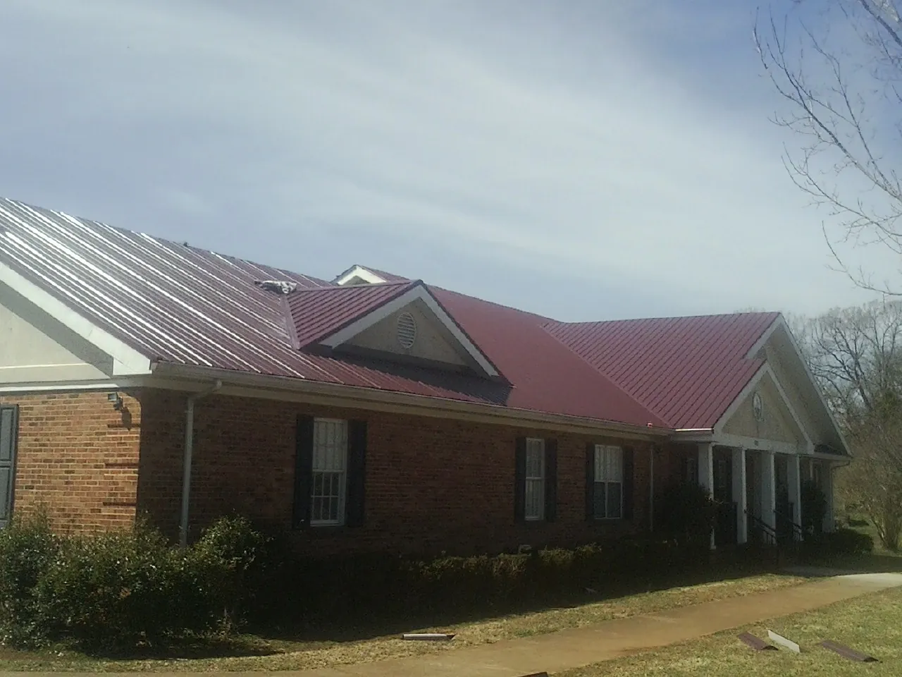 Red metal roof with gabled entries on a long brick building, from a Hail Damage Roof Repair job in Shawano