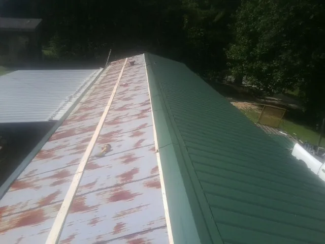 Old rusted panels beside newly installed green metal roofing — Wind Damage Roof Repair by Roofing Brothers in Shawano