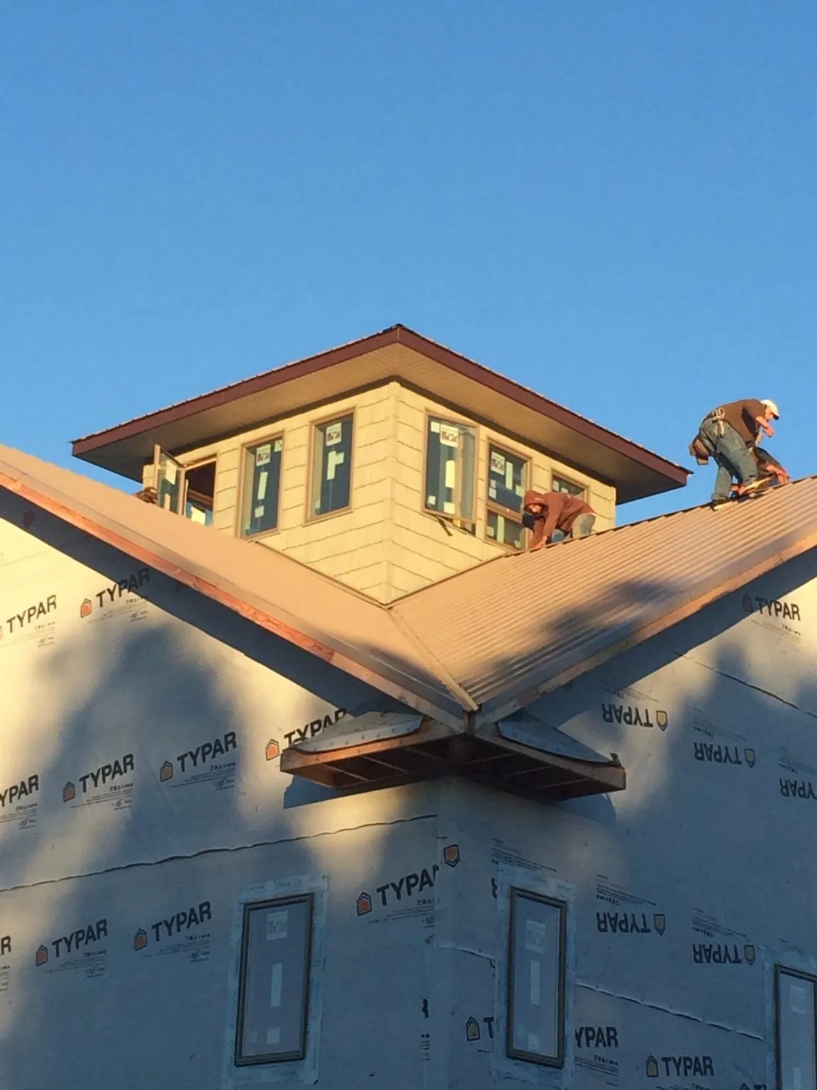 Roofers working around a rooftop cupola on a new metal roof at sunset — Roof Waterproofing in Shawano by Roofing Brothers